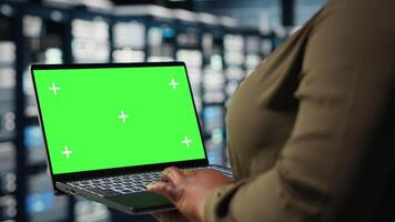 dati centro Admin usi isolato schermo il computer portatile per sviluppare disastro recupero piani, minimizzando tempi di inattività. donna nel server azienda agricola valorizzare dati protezione protocolli utilizzando modello taccuino, telecamera B video