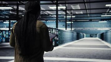 ingénieur dans Les données centre en utilisant tablette à déployer sécurise serveur architecture. africain américain femme dans serveur centre en utilisant dispositif à faire sortir de la cyber-sécurité cadre, caméra une video