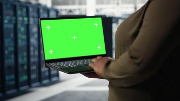 Data center expert monitors data center metrics on isolated screen laptop to enhance operational effectiveness. Server hub worker uses analytics on mockup notebook to predict performance, camera B video