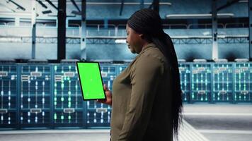 software desarrollador a trabajo utilizando verde pantalla tableta en datos centrar a cheque hardware para sistema estabilidad. africano americano mujer utilizando croma llave dispositivo a supervisar servidor granja, cámara un video