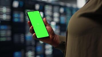 Server hub software developer uses green screen smartphone to watch tutorial on how to upgrade rig. African american woman in data center follows guide on mockup phone to improve speed, camera B video