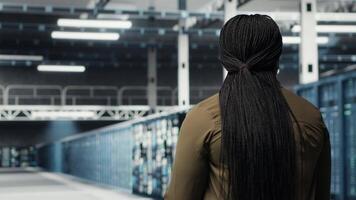 administration i data Centrum arbetsplats övervaka stor skala den elektronik till upprätthålla sömlös operationer. kvinna gående i hög tech server rum, håller på med nätverk förvaltning för ökade upptid, kamera b video