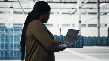 Techniker mit Laptop Spaziergänge durch Daten Center Server Reihen, Umsetzung fortgeschritten Leistung Verwaltung Lösungen. Arbeiter mit Notizbuch zu überwachen Server Hub, reduzieren Energie Verbrauch, Kamera b video