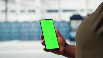 Close up of admin working in data center using isolated screen smartphone to optimize network infrastructure. Server farm worker diagnosing hardware malfunctions using mockup mobile phone video