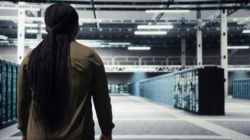 beheerder in gegevens centrum werkplaats toezicht houden op groot schaal het elektronica naar in stand houden naadloos activiteiten. vrouw wandelen in hoog tech server kamer, aan het doen netwerk beheer voor is gestegen beschikbaarheid, camera een video