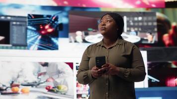 kvinna använder sig av smartphone omgiven förbi kurerad rekommendationer medan bläddring strömning tjänster. person njuter fri tid bläddring favorit uppkopplad clips på telefon, kamera b video