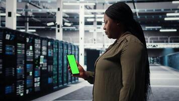 software desarrollador utilizando aplicación en Bosquejo teléfono a cheque servidor cubo energía consumo. africano americano mujer utilizando verde pantalla teléfono inteligente en datos centrar a hacer engranaje chequeo, cámara un video