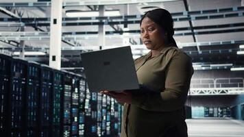 ingeniero utilizando ordenador portátil en datos centro, integrando nuevo tecnologías y sistemas trabajador utilizando cuaderno a supervisar servidor centro, asegurando conformidad con industria estándares, cámara un video