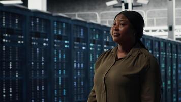 portret van glimlachen beheerder wandelen in gegevens centrum, toezicht houden op groot schaal het infrastructuur naar in stand houden naadloos activiteiten. gelukkig server boerderij werknemer verheugd door is gestegen beschikbaarheid, camera b video