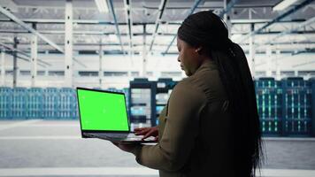 Techniker mit Grün Bildschirm Laptop im Daten Center Umsetzung fortgeschritten Leistung Verwaltung Lösungen. Mitarbeiter mit Attrappe, Lehrmodell, Simulation Notizbuch zu überwachen Server Hub, reduzieren Energie Verbrauch, Kamera ein video