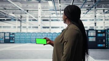 Server hub system administrator uses green screen smartphone to watch tutorial on how to upgrade rigs. Data center employee following guide on mockup mobile phone to improve speed, camera A video
