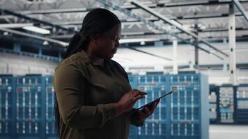 Developer in data center using tablet to upgrade systems for increase in clients workload capacity. IT expert in server farm configuring hardware, improving data processing speed, camera B video