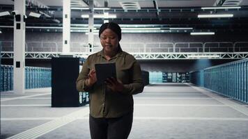 Ingenieur mit Tablette Spaziergänge durch Daten Center Server Reihen, Umsetzung fortgeschritten Leistung Verwaltung Lösungen. es Fachmann mit Gerät zu überwachen Server Hub, reduzieren Energie Verbrauch, Kamera ein video
