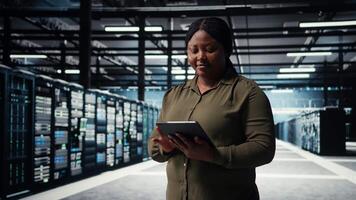 Programmer in data center using tablet to upgrade servers for increase in clients workload capacity. IT specialist in server farm configuring hardware rigs, improving data processing speed, camera A video