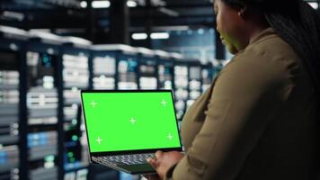 Developer in data center using green screen laptop to upgrade systems for increased stability. IT expert in server farm configuring hardware with mockup notebook for optimum performance, camera B video