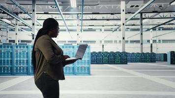 Techniker mit Laptop Spaziergänge durch Daten Center Server Reihen, Umsetzung fortgeschritten Leistung Verwaltung Lösungen. Arbeiter mit Notizbuch zu überwachen Server Hub, reduzieren Energie Verbrauch, Kamera ein video