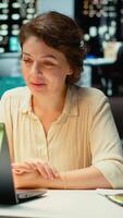 Vertical Professional woman sits in front of laptop during a teleconference, engaged in digital discussion. Interacting with participants, demonstrating adaptability in networking session. Camera B. video