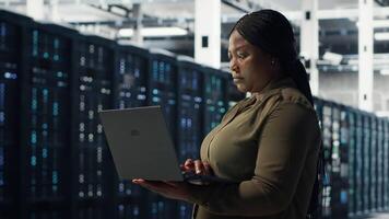 ingeniero utilizando ordenador portátil en datos centro, integrando nuevo tecnologías y sistemas trabajador utilizando cuaderno a supervisar servidor centro, asegurando conformidad con industria estándares, cámara si video