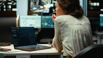 professionell arbetstagare i kontor monitorer stock trender och ljusstake diagram på bärbar dator, använder sig av data analys, prognostisering och finansiera strategi till optimera handel och uppnå inkomst mål. kamera b. video