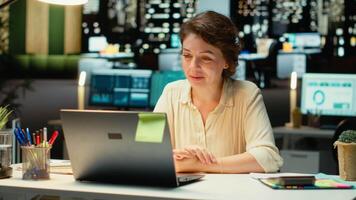 professionell kvinna sitter i främre av bärbar dator under en telefonkonferens, engagerad i digital diskussion. interagera med deltagare, demonstrera anpassningsförmåga i nätverkande session. kamera b. video