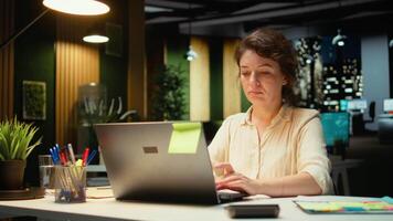 kvinna anställd korrekturläsning en dokumentera innan transkribering på anteckningsbok, handskriven anteckningar på papper efter timmar. kvinna engagerad i dokumentera Viktig idéer från arkiveras Rapportera. kamera a. video