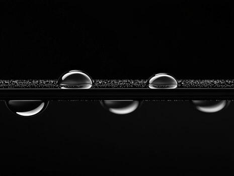 Monochrome image of clear water drops suspended on a thin dark line against a black background photo
