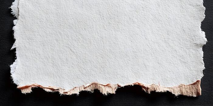 A textured white paper with torn ragged edges is placed on a dark background showing a peach colored layer underneath photo