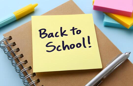 A close-up view of a yellow sticky note with the phrase Back to School written on it, affixed to a spiral-bound notebook. photo
