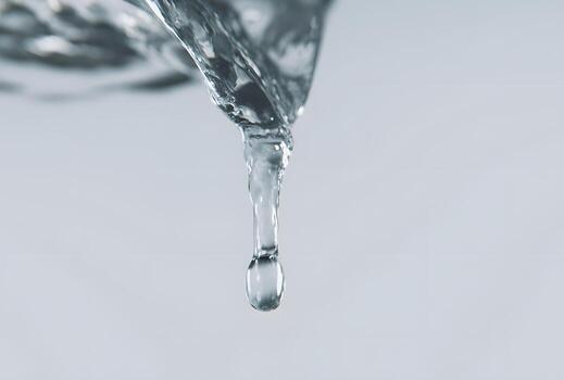 A close-up view of a single water droplet falling, showcasing the intricate details of its form and texture against a plain background. photo