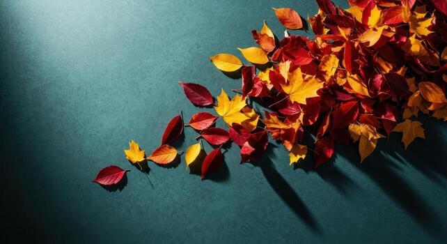 Vibrant autumn leaves falling across a dark teal textured surface with dynamic shadows photo