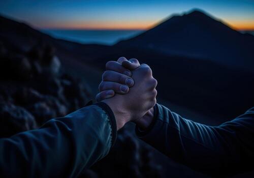 Climbers hands clasped in strong support against a dramatic mountain landscape at twilight photo