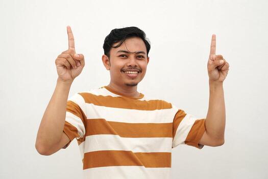 Young Asian man in white and brown striped t-shirt smiling and pointing up with both index fingers enthusiastically, posing with a cheerful and eye-catching gesture against a white background., photo