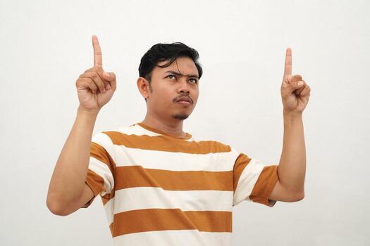 Young Asian man in white and brown striped tshirt smiling and pointing up with both index fingers enthusiastically, posing with a cheerful and eye-catching gesture against a white background photo
