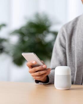 Focused person using smartphone and connecting to modern wireless smart speaker. Voice assistant technology for smart home creating calm and convenient lifestyle photo
