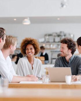 Smiling group of diverse colleagues sharing ideas over lunch. happy professional team in meeting discussing project at modern office cafeteria with laptop photo