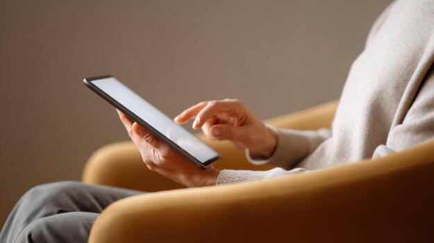 Relaxed person using phone while sitting in yellow armchair at home. Closeup of hand scrolling on screen, using modern technology to browse internet photo