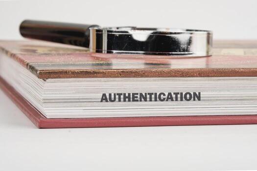 A close-up view highlights the word authentication printed on the edge of a book alongside a magnifying glass, symbolizing the importance of security and verification in digital identity photo