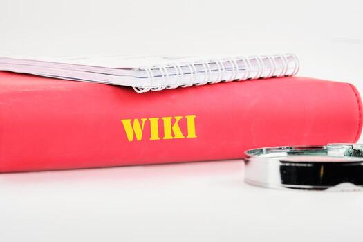 A red binder titled Wiki is placed alongside a spiral notebook and a magnifying glass, symbolizing the processes of research and learning in technology concepts photo
