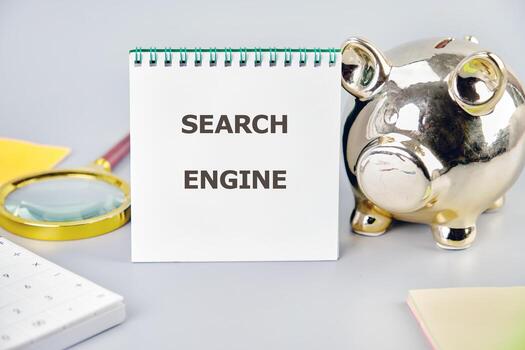 A notepad displaying the term search engine is placed alongside a golden piggy bank and a magnifying glass, symbolizing business innovation photo