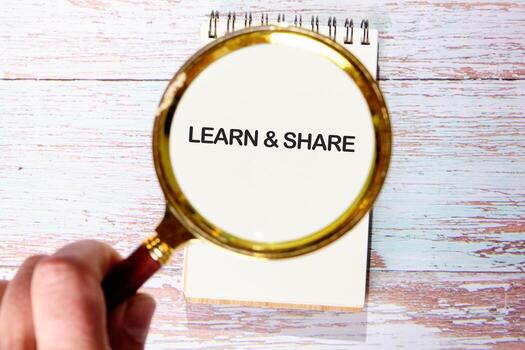A hand with a magnifying glass over a notepad reading learn and share, highlighting the value of knowledge in business finance photo