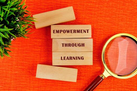 The message connect through learning. EMPOWERMENT THROUGH LEARNING assembled from wooden blocks in composition with magnifying glass and green plant on orange background, top view photo