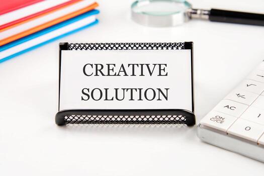 Create your Brand symbol. Concept words CREATIVE SOLUTION on a business card in a composition with a magnifying glass, notebooks, a calculator on a white background photo