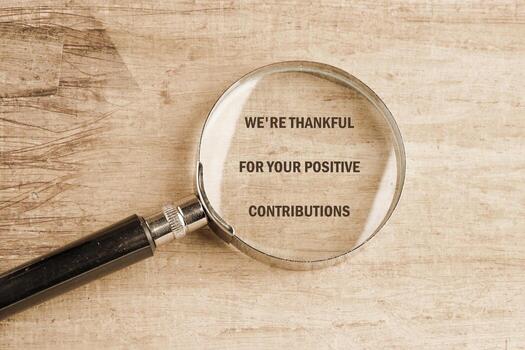 A magnifying glass rests on a textured wooden surface, magnifying the message expressing gratitude for positive contributions. This setting creates a thoughtful atmosphere of appreciation photo
