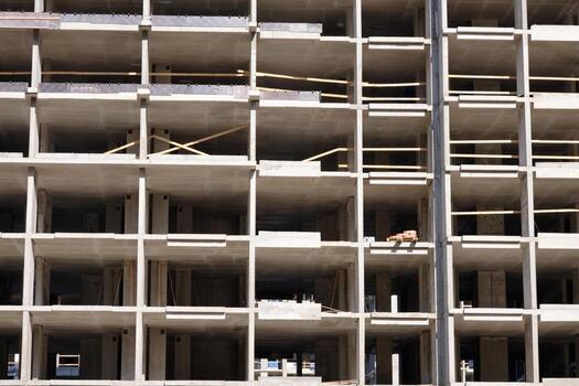 A tall multi story building is being constructed with open concrete floors and wooden supports, illuminated by sunlight. The structure awaits further development photo