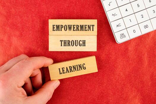 Through education and learning to success concept. EMPOWERMENT THROUGH LEARNING words assembled from blocks in a composition with part of a white calculator and a hand, top view photo