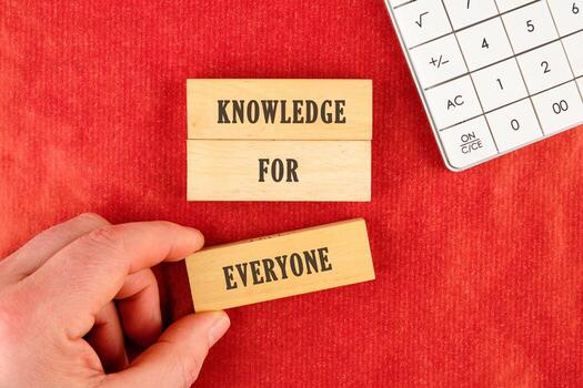 Learning for Everyone concept. Words KNOWLEDGE FOR EVERYONE assembled from blocks in a composition with part of a white calculator and a hand, top view photo