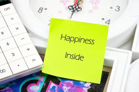 A lime-green sticky note with Happiness Inside sits by a calculator and a clock on a desk The clock shows the passing time, hinting at strategies, business, and motivation photo