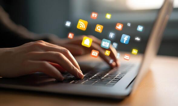 A person typing on a laptop with social icons coming out of the keyboard photo