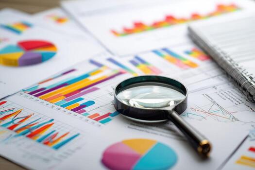 Business charts and graphs with magnifying glass on top of paper photo