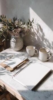 A white desk with a notebook, coffee cup and vase photo